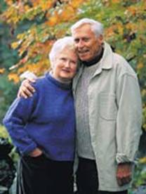 Older couple standing in front of autumn leaves.