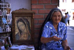 photo of old elderly mexican catholic woman selling religious items souvenirs virgin mary street vendor peddler poor scenery mexico travel concept 