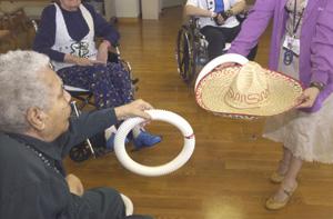 At Cooper River West nursing home in Pennsauken, Herminia Figueroa is set to toss a ring onto a sombrero held by Giselle Maldonado, a therapeutic recreational assistant. The home, owned by Genesis HealthCare Corp., offers Spanish-language exercise classes, games and special meals.