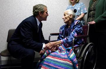 President sits to speak with a wheelchair-bound elderly woman.